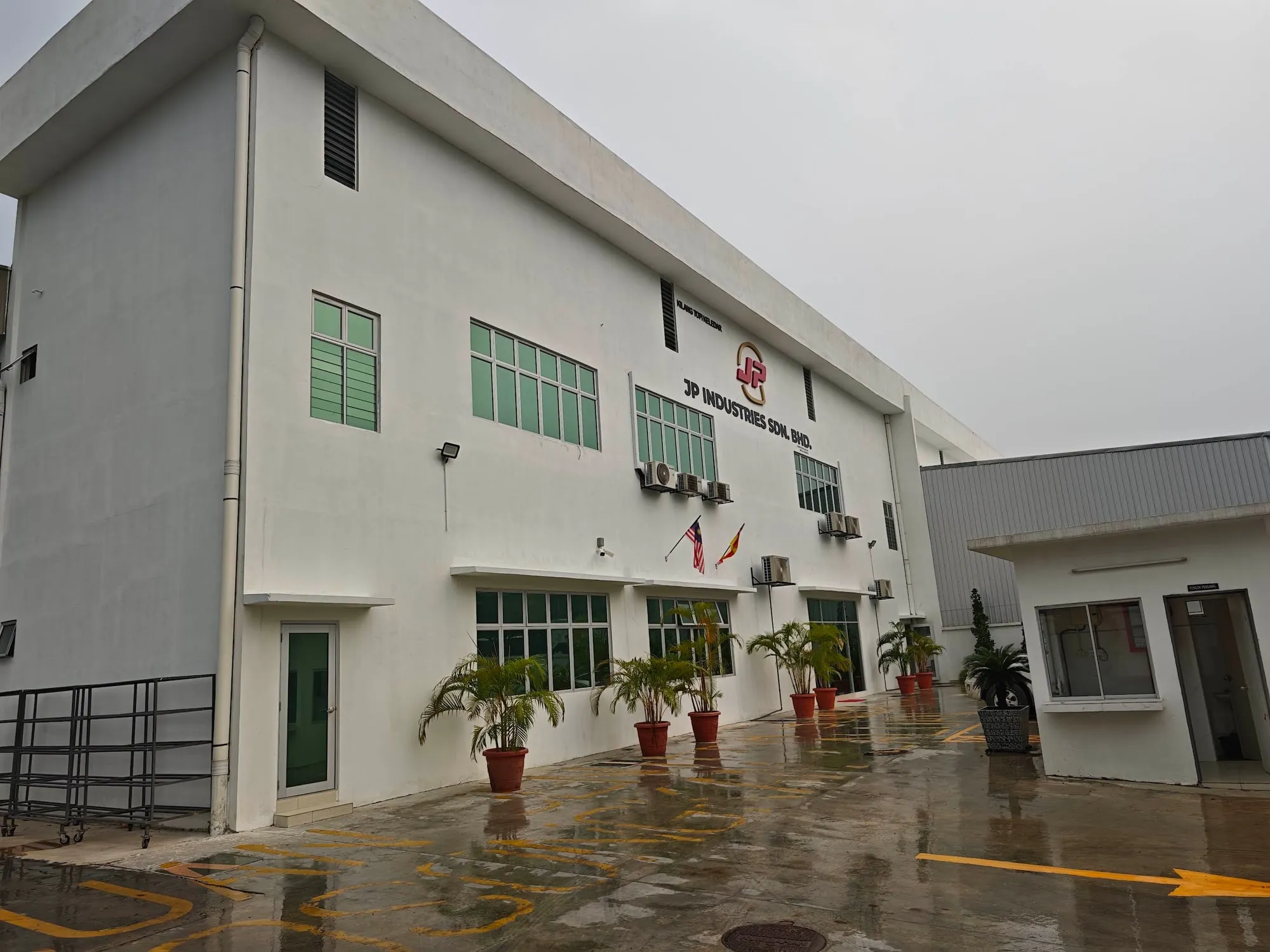 White three-storey factory office block with a guardhouse and paved compound